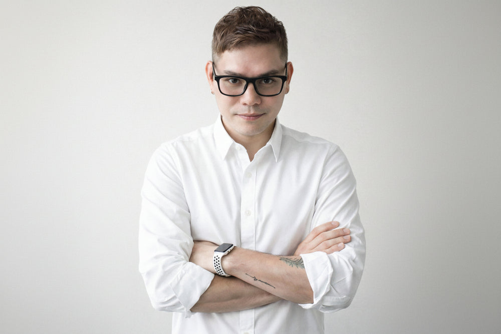 Man wearing a white shirt and glasses with arms crossed on a plain background